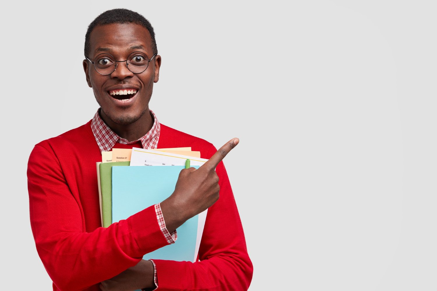 positive-college-student-has-dark-skin-carries-folders-book-points-with-cheerful-expression-aside-has-toothy-smile